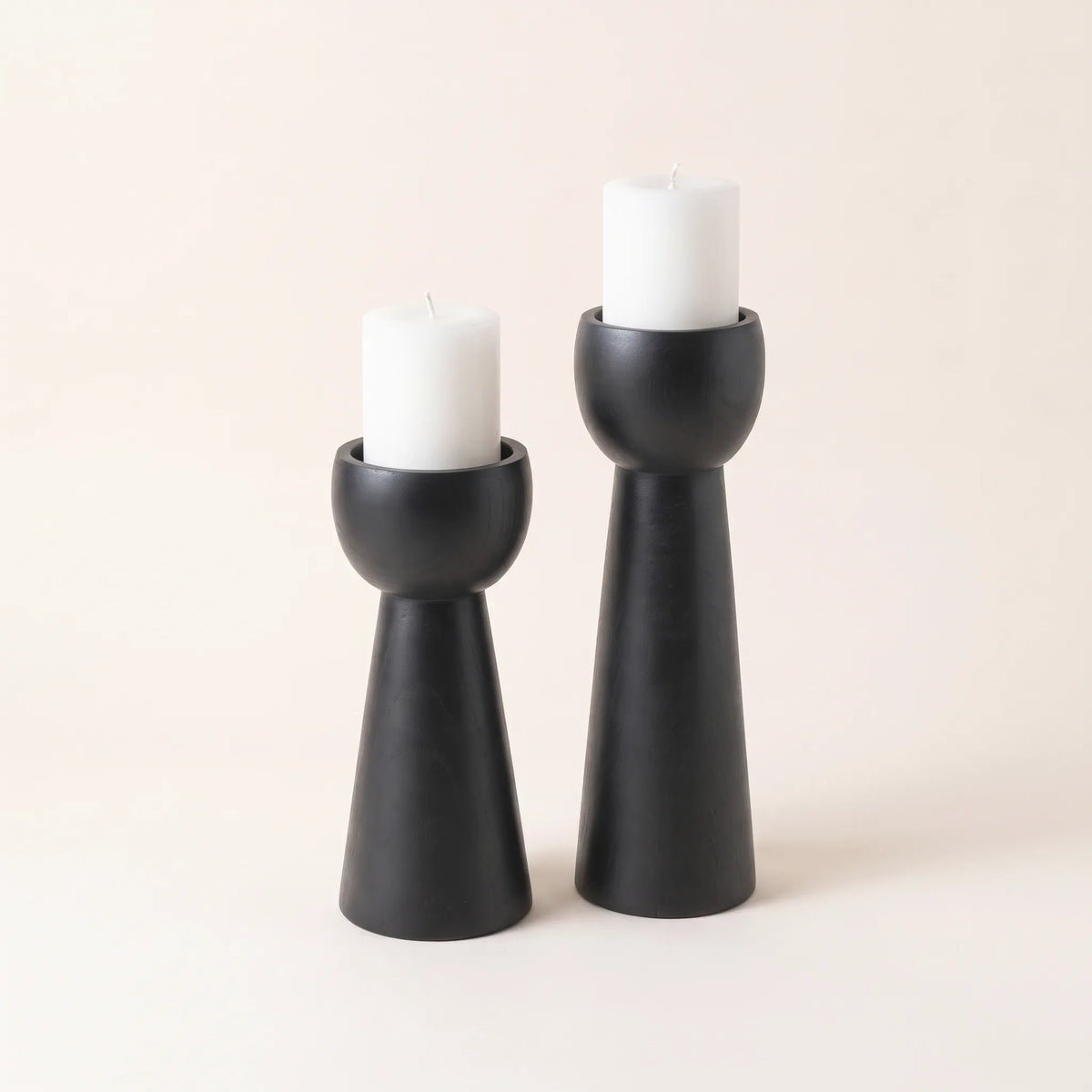 Candelabros de madera negro mate con velas de pilar crema sobre fondo claro