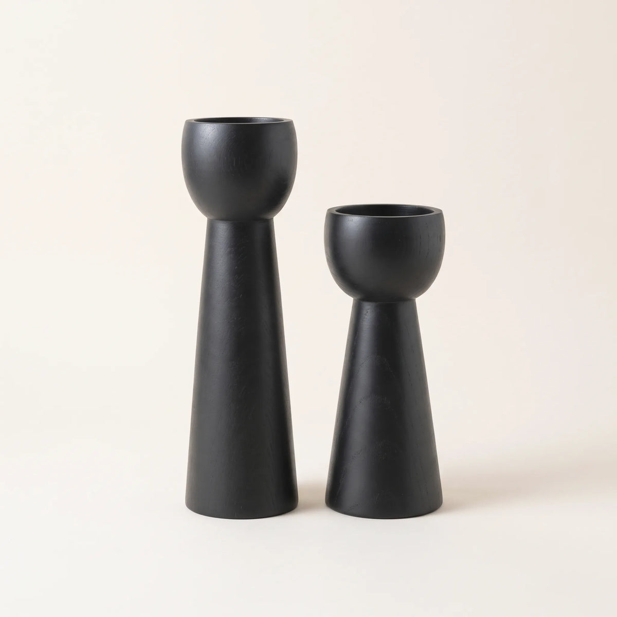 Dos candelabros de madera negro mate con base cónica y copa redonda sobre fondo claro