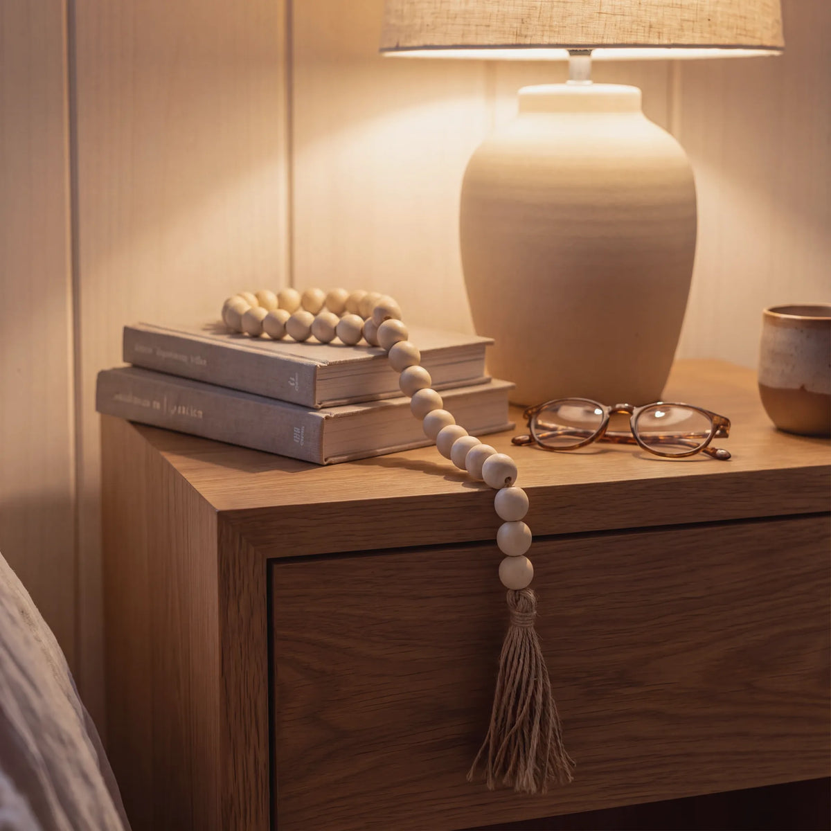 Guirnalda de cuentas de madera crema junto a una lámpara sobre una mesa de noche de madera
