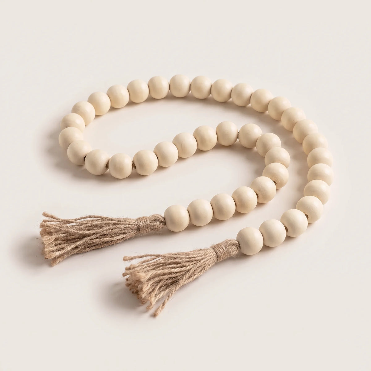Guirnalda de cuentas de madera color crema con borlas de yute sobre fondo claro