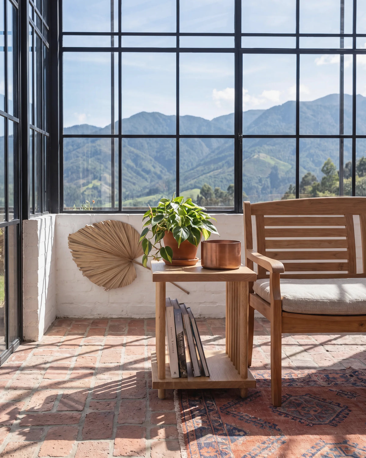 Mesa auxiliar de roble con libros junto a un sofá en una terraza acristalada de La Calera
