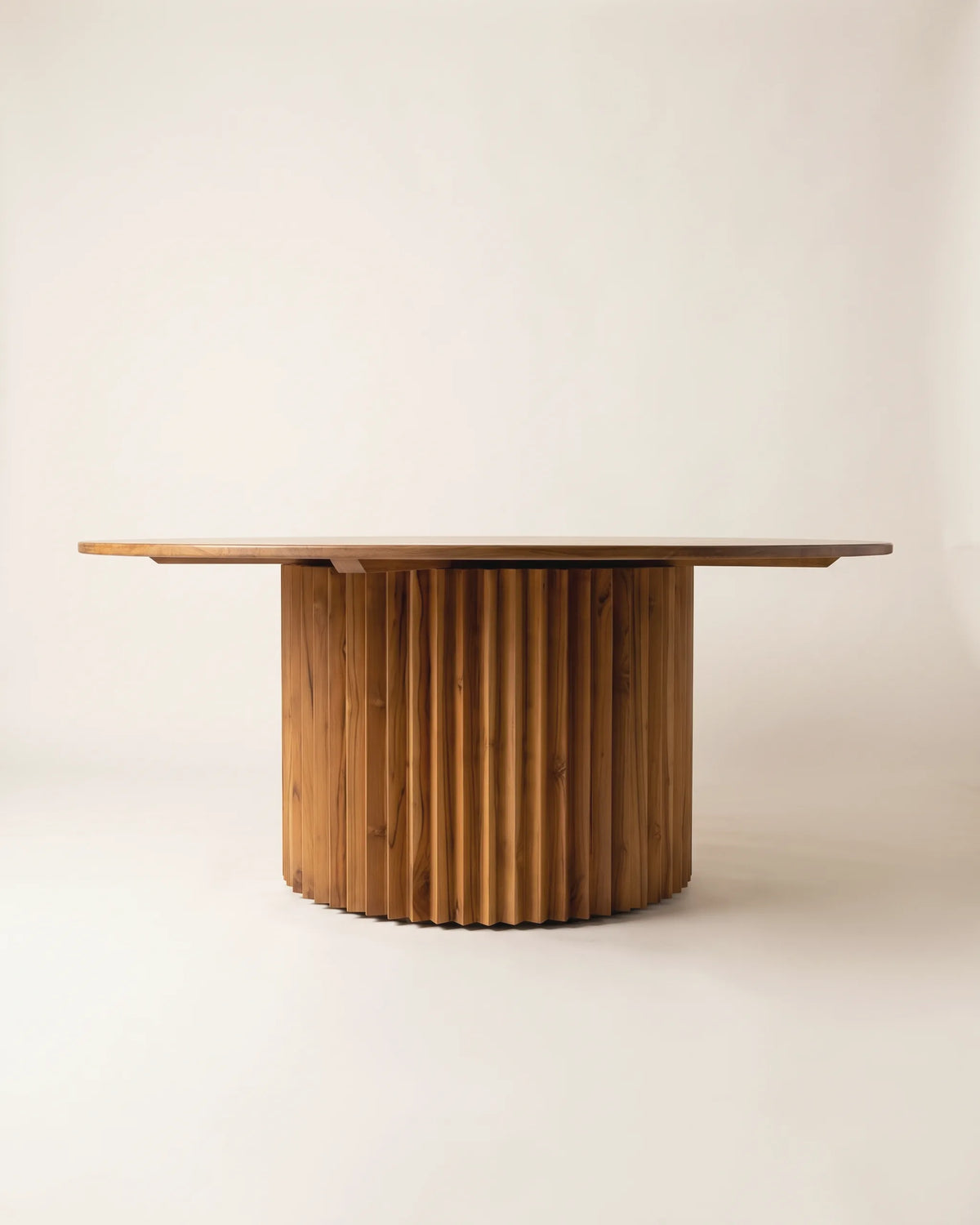 Mesa de comedor redonda de teca de 180 cm con base cilíndrica de listones sobre fondo claro