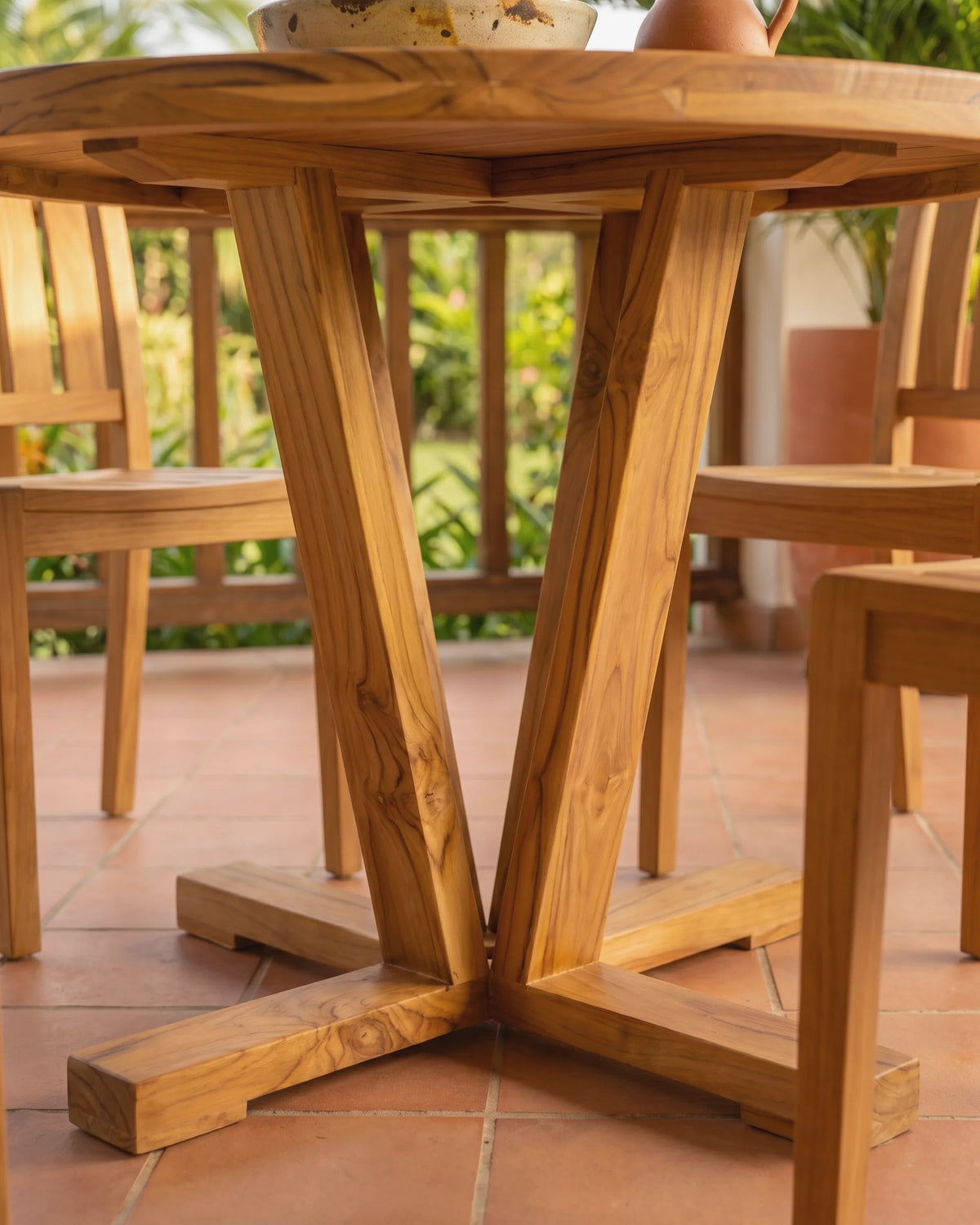 Patas en ángulo de teca maciza unidas al pie en cruz de una mesa de comedor redonda