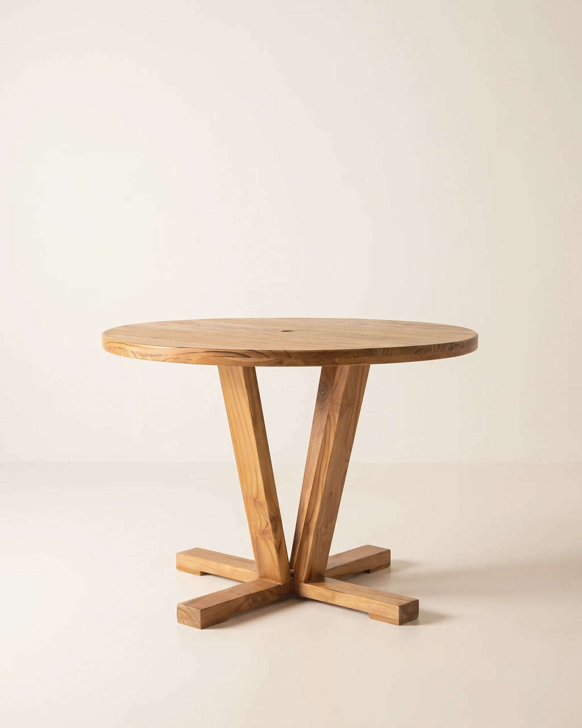 Mesa de comedor redonda en teca maciza de 90 cm con patas en ángulo y pie en cruz sobre fondo claro