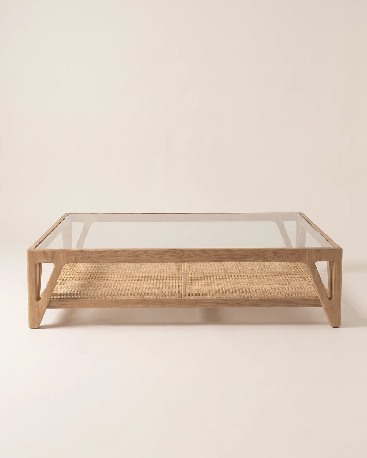 Mesa de centro de roble con tapa de vidrio, entrepaño de esterilla y patas con corte en V sobre fondo claro