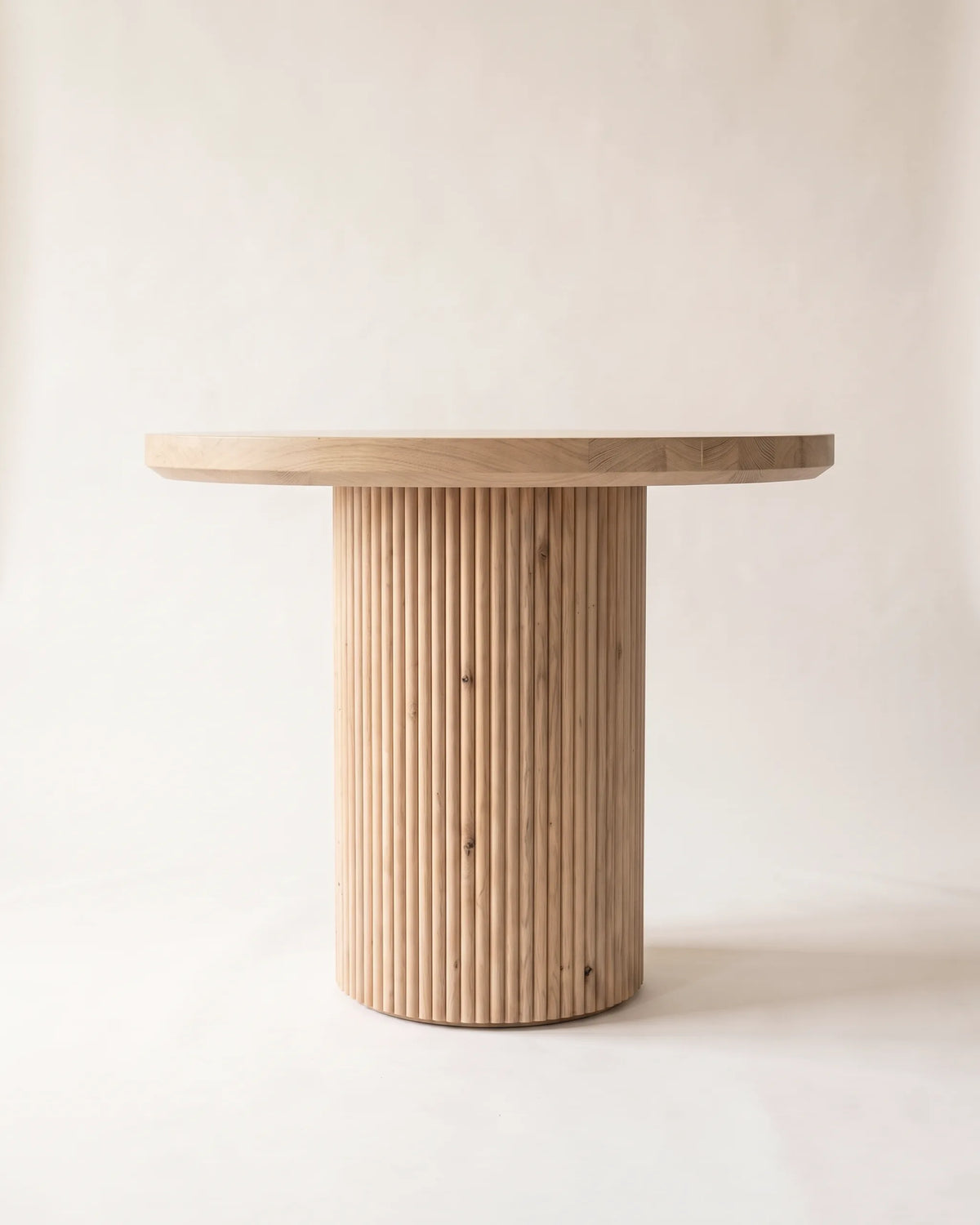 Mesa de comedor redonda de roble de 90 cm con pedestal de listones verticales sobre fondo claro