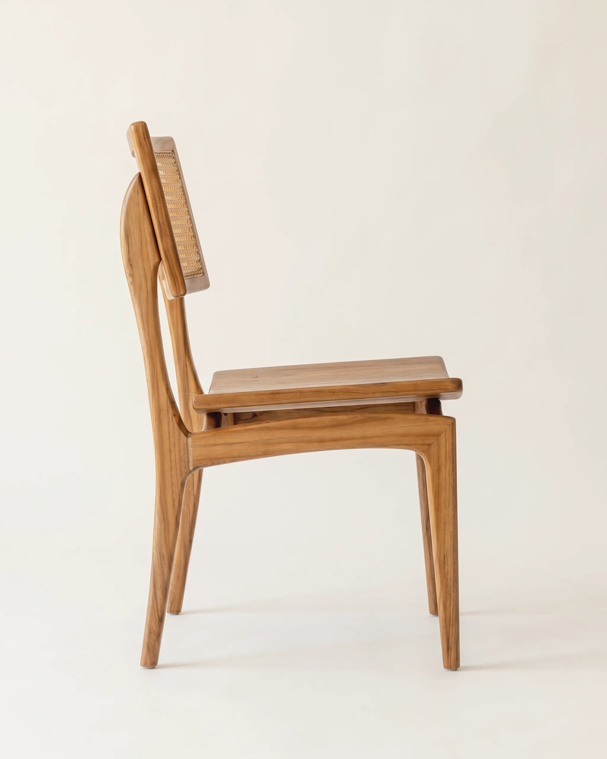 Silla de comedor Menina de teca vista de lado con asiento flotante sobre fondo claro
